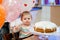 Adorable little baby girl celebrating first birthday. Baby eating marshmellows decoration on homemade cake, indoor