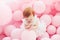 Adorable, little baby girl is delighted by standing among pastel pink balloons on the party