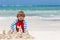 Adorable little blond kid boy having fun on tropical beach of carribean island. Excited child playing and building sand