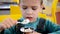 Adorable little boy in a businessman`s business suit in a hurry eating ice cream at restaurant during lunch.