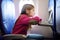 Adorable little child traveling by an airplane. Girl sitting by aircraft window and reading her ebook during the flight.