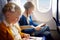 Adorable little children traveling by an airplane. Girl sitting by aircraft window and reading her ebook during the flight. Travel