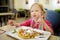 Adorable little girl eating bubble waffle with fruits, chocolate and marshmallows. Children eating sweets.