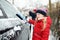 Adorable little girl helping to brush a snow from a car. Mommy`s little helper.