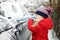 Adorable little girl helping to brush a snow from a car. Mommy`s little helper.