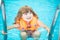 Adorable little girl with inflatable life vest having fun in the pool