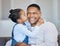Adorable little girl kissing her dad on the cheek. African american man laughing and looking joyful while receiving love