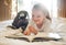 Adorable little girl reading book while lying on bed with teddybear. Cute kid reading with finger while relaxing in her