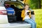 Adorable little girl ready to go on vacations with her parents. Kid sitting in a car trunk and reading her ebook.