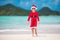 Adorable little girl in Santa hat on tropical beach