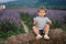 Adorable little girl sits on hay by the farm. Background of summer lavender field. Cute girl in striped t-shirt and blue