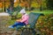 Adorable little girl sitting on the bench with lunchbox and having picnic on a fall day