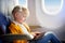 Adorable little girl traveling by an airplane. Child sitting by aircraft window and using a digital tablet during the flight. Trav