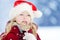 Adorable little girl wearing Santa hat having huge striped Christmas lollipop on beautiful winter day