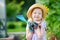 Adorable little girl wearing straw hat and childrens garden gloves playing with her toy garden tools in a greenhouse