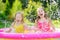 Adorable little girls playing in inflatable baby pool. Happy kids splashing in colorful garden play center on hot summer day.