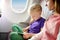 Adorable little girls traveling by an airplane. Children sitting by aircraft window and using a digital tablet during the flight.