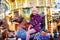 Adorable little kid girl riding on a carousel horse at Christmas funfair or market, outdoors.