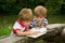 Adorable Little Twin Brothers Looking and Pointing at Very Interesting Picture in the Book Near the Beautiful Lake