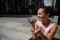 Adorable mixed race woman recording a voice message on smartphone, resting on steps on the urban buildings background