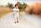 Adorable redhead toddler baby boy in jumpsuit running along rural summer road in sunburned field