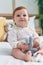 Adorable redhead toddler holding doll sitting on bed at bedroom