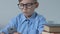 Adorable school boy in glasses playing smartphone game in classroom during break