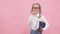 Adorable schoolgirl with funny pigtails on head holding textbooks in hands smiling in camera and fixing glasses finger