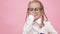 Adorable schoolgirl with funny pigtails on head holding textbooks in hands smiling in camera and fixing glasses finger