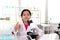 Adorable schoolgirl in lab coat doing science experiments, young scientist and giving thumb, using microscope and learning science