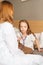 Adorable sick little girl playing with stethoscope while lying in bed in bedroom during visit of pediatrician at medical