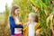 Adorable sisters playing in a corn field on beautiful autumn day. Pretty children holding cobs of corn. Harvesting with kids.