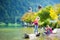 Adorable sisters playing by Konigssee lake in Germany on warm summer day. Cute children having fun feeding ducks and throwing ston