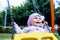 Adorable smiling baby girl with kerchief enjoying a swing ride on a playground in a park on a nice sunny summer day