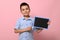 Adorable smiling boy pointing on an empty blank board with a chalk. Space for text on a chalkboard. Pink background with copy