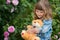 Adorable smiling girl with teddy bear in park with pink rose.