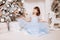 Adorable smiling little girl in festive princess blue dress is looking in camera in cozy room decorated lighting