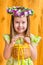 Adorable smiling little girl with long blond hair wearing floral head wreath and holding wicker basket with yellow eggs