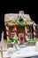 Adorable snow-covered homemade gingerbread house, a sprig of Christmas tree and a sugar mastic snowman on dark background
