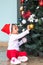 An adorable South Asian toddler hanging a Christmas ball on the tree indoors