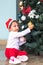 An adorable South Asian toddler hanging a Christmas ball on the tree indoors