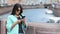 Adorable stylish girl taking photo using smartphone from embankment at historical cityscape