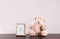 Adorable teddy bear and frame with cute picture on table against light background, space for text.