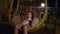 Adorable teenage girl using smartphone and resting in cocoon swing chair