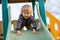 Adorable toddler boy having fun and sliding on outdoor playground