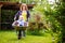 Adorable toddler boy having fun in a wheelbarrow pushing by mum in domestic garden