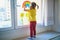 Adorable toddler girl attaching drawing of rainbow to window glass as sign of hope