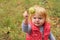 Adorable toddler girl with blond hair holding chestnut; autumn background