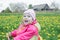 Adorable toddler girl driving pink and yellow tricycle across the spring blossoming dandelions meadow