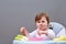 Adorable toddler girl is having fun while eating on greyish background